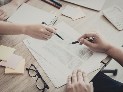 Zwei Mitarbeitende sitzen an einem Tisch im Büro und prüfen Dokumente